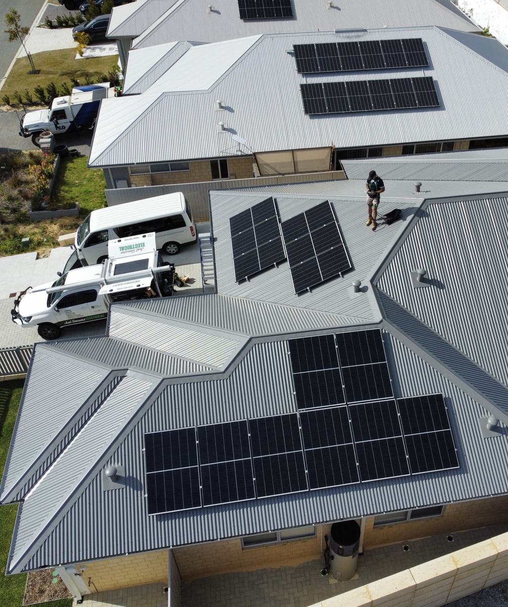 Drone view of a grey metal roof with solar panels and an electrician on the roof