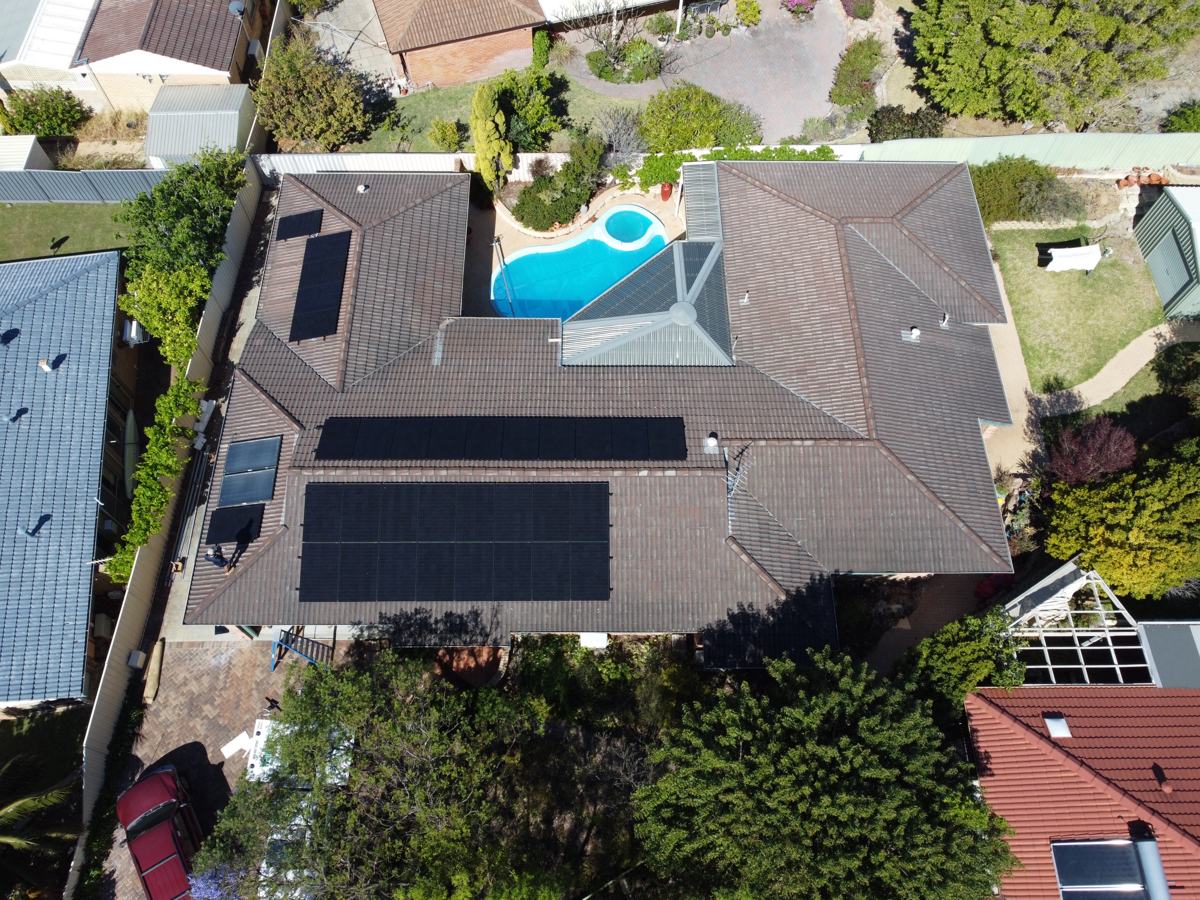 Drone view of a house with several solar arrays and a pool