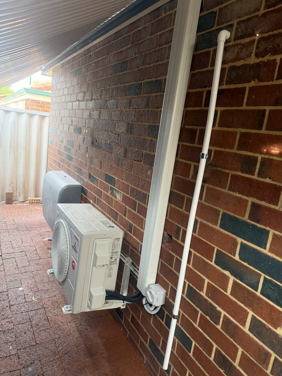 Outdoor air conditioning unit on a brick wall with white conduit and isolator