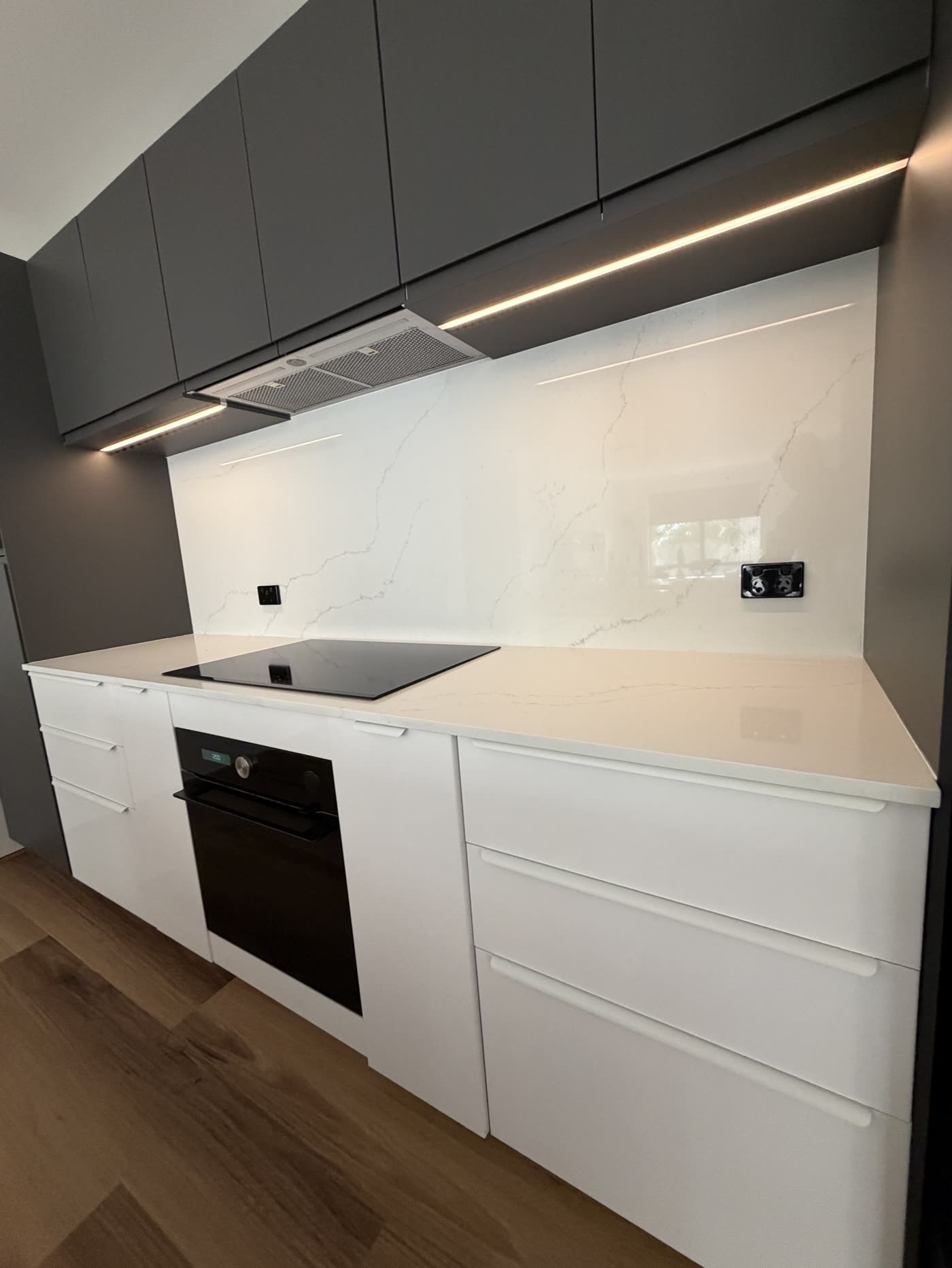 Modern kitchen with LED strip lighting under dark overhead cabinets and a marble splashback