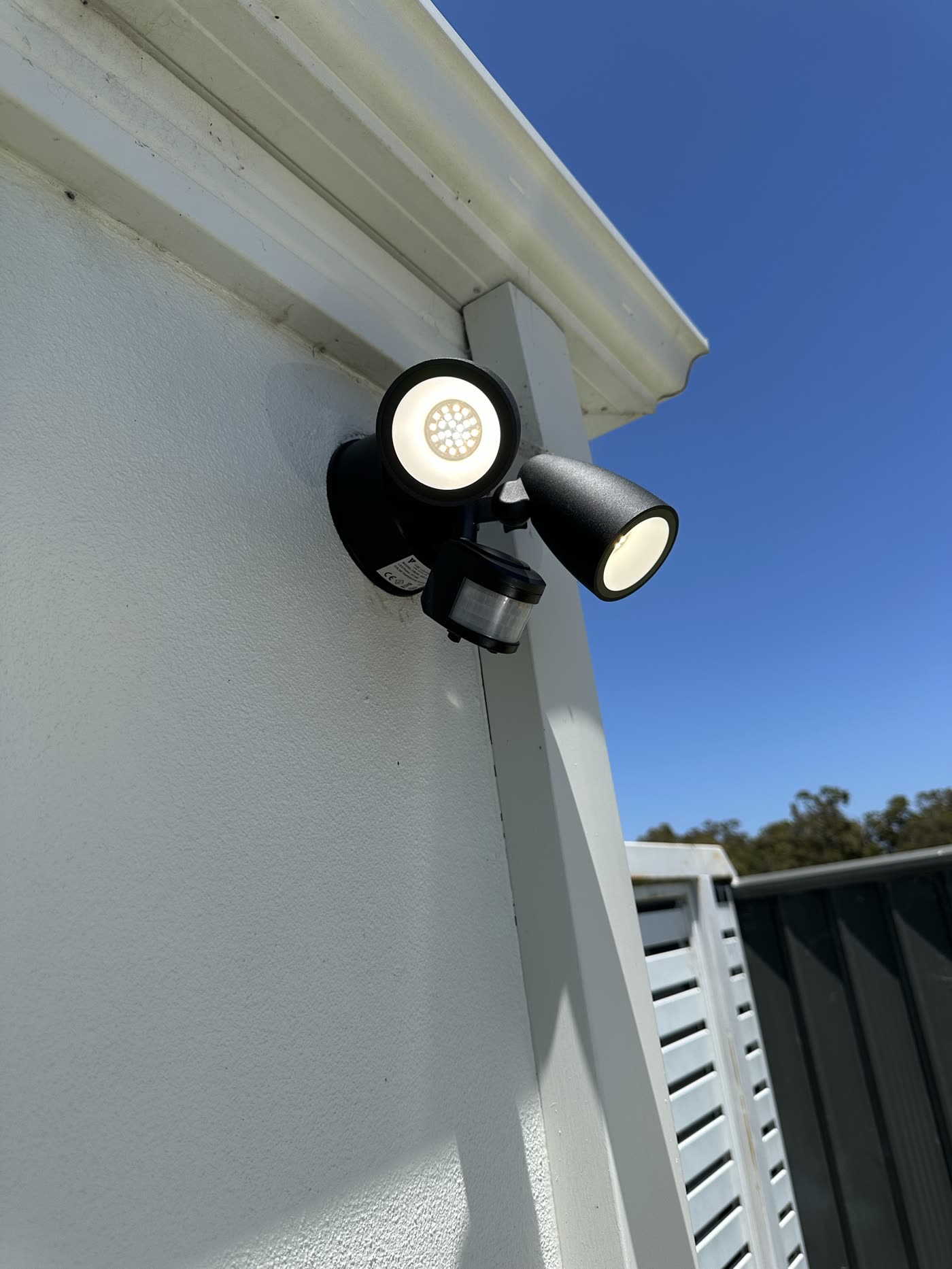 Black twin sensor flood light mounted under the eaves