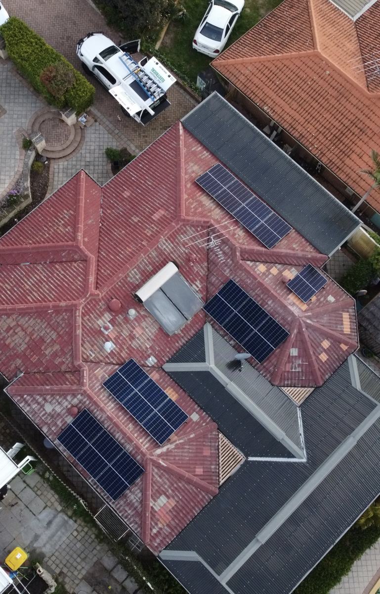 Drone view of a red tiled roof with several solar arrays and a work ute