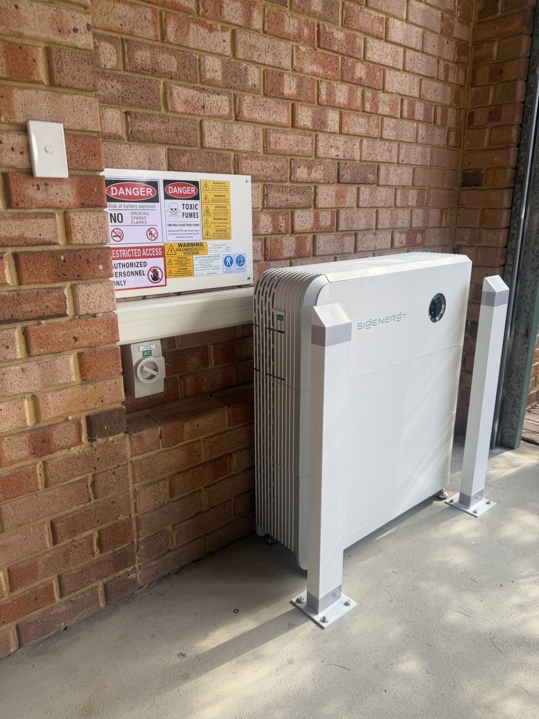 Wall-mounted home battery with protective posts and warning signage
