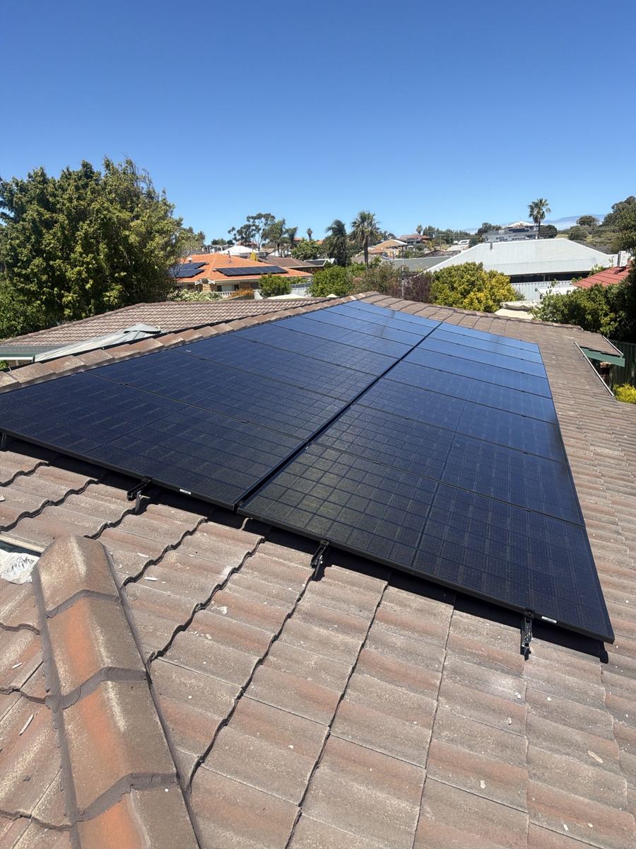 Black solar panels on a tiled roof under a clear blue sky