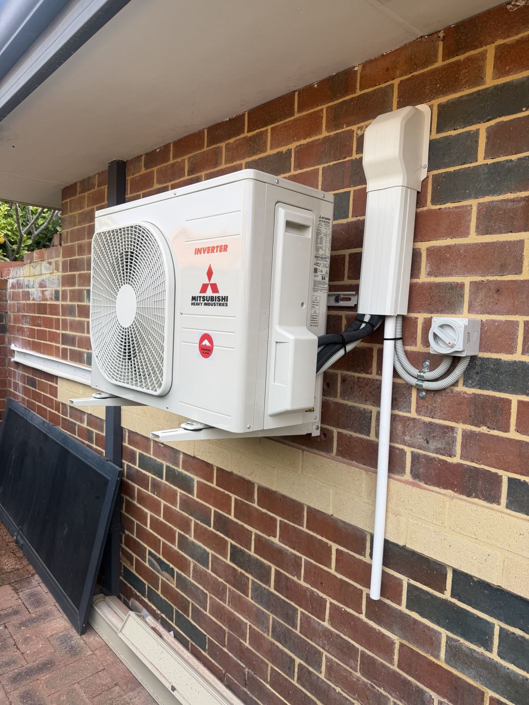 Outdoor air conditioning unit on a brick wall with isolator and conduit