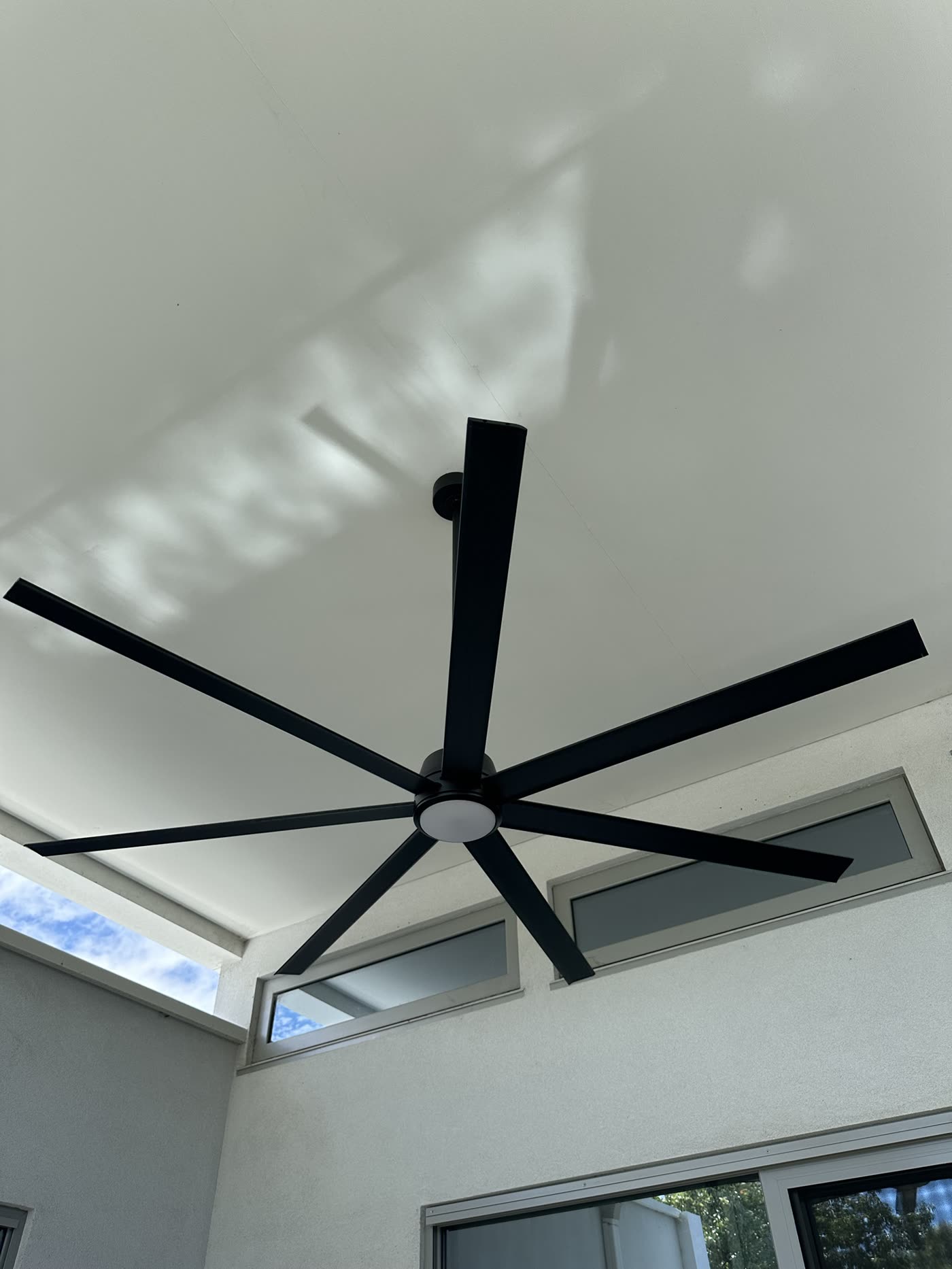 Large black seven-blade ceiling fan with an LED light on an outdoor patio