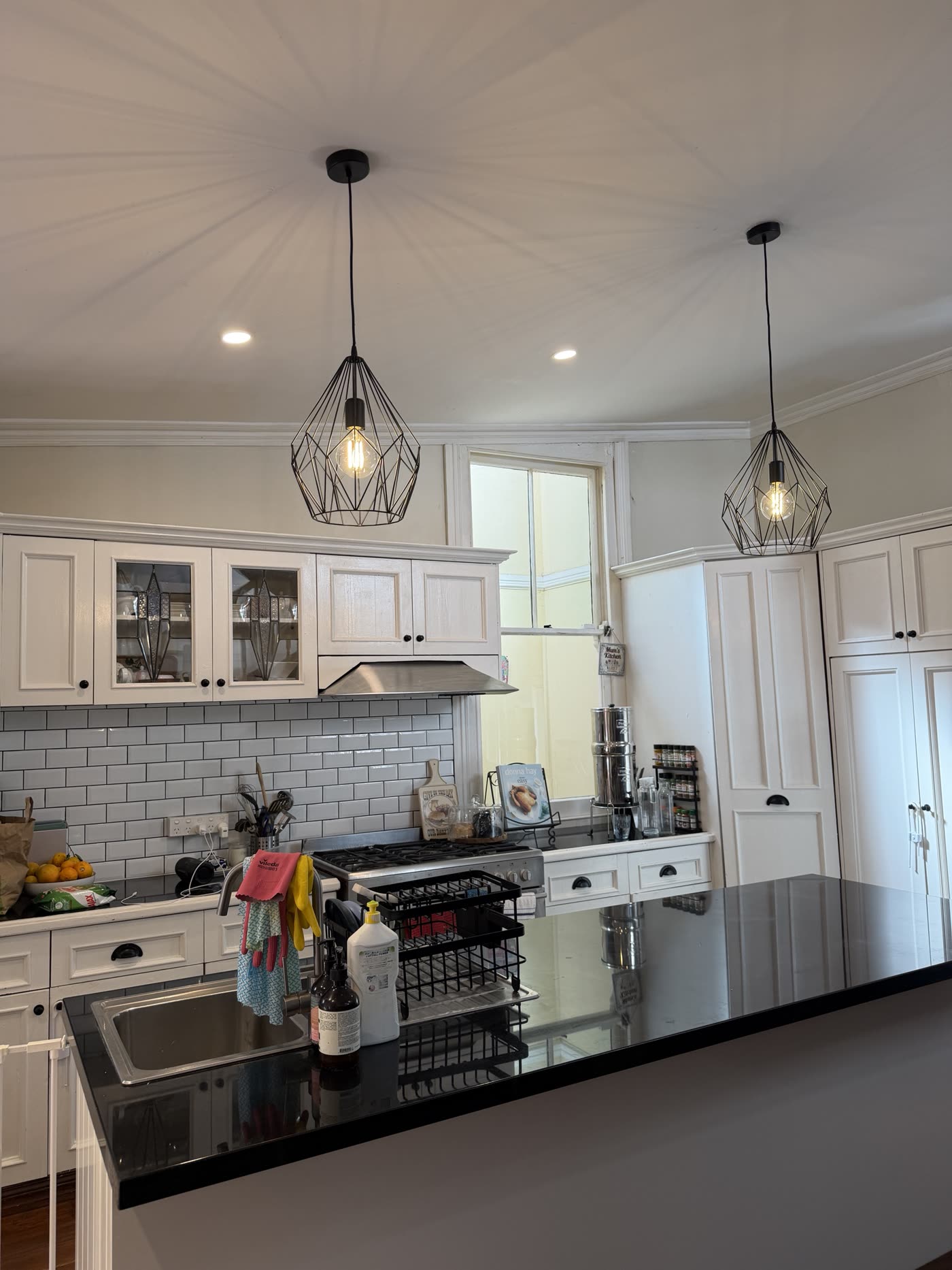 Kitchen with two black geometric cage pendants and downlights over a black stone island