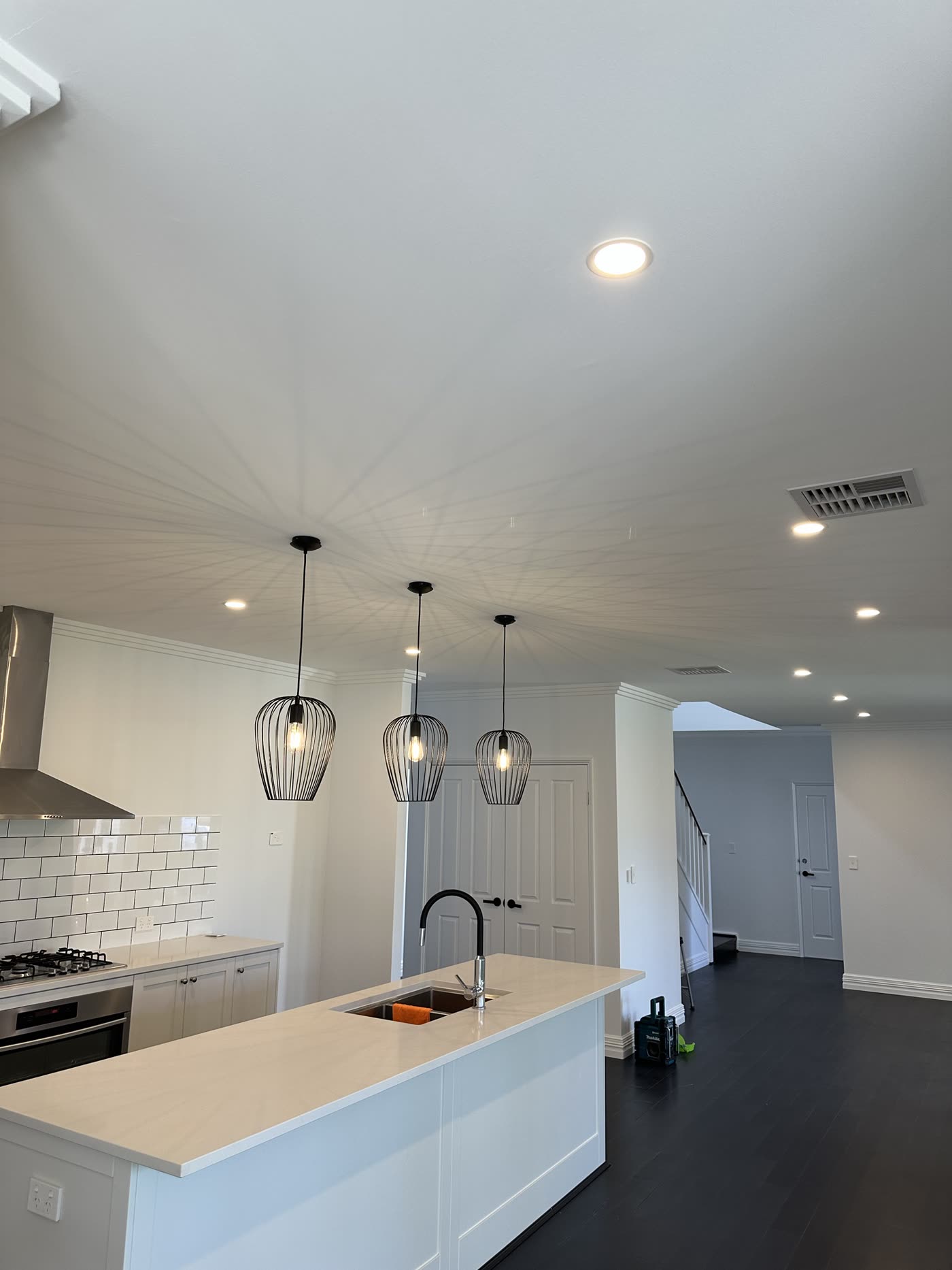 Three black cage pendants over a white stone kitchen island with downlights
