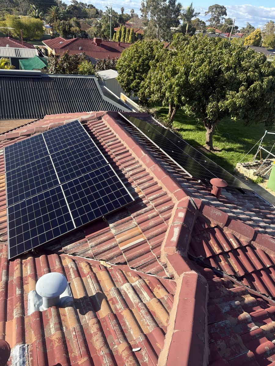 Solar panels on a red tiled roof beside a tree-lined backyard