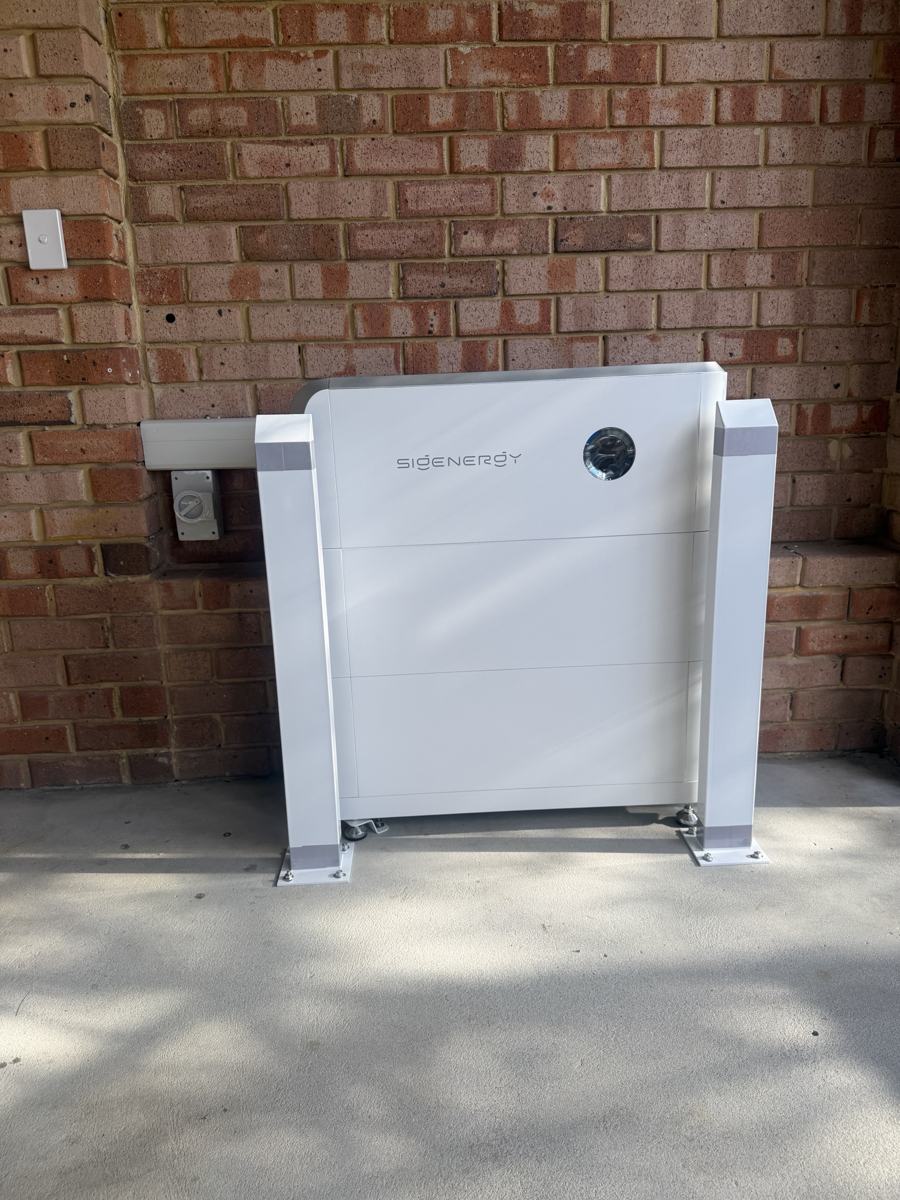 Wall-mounted home battery with protective posts beside an isolator on a brick wall