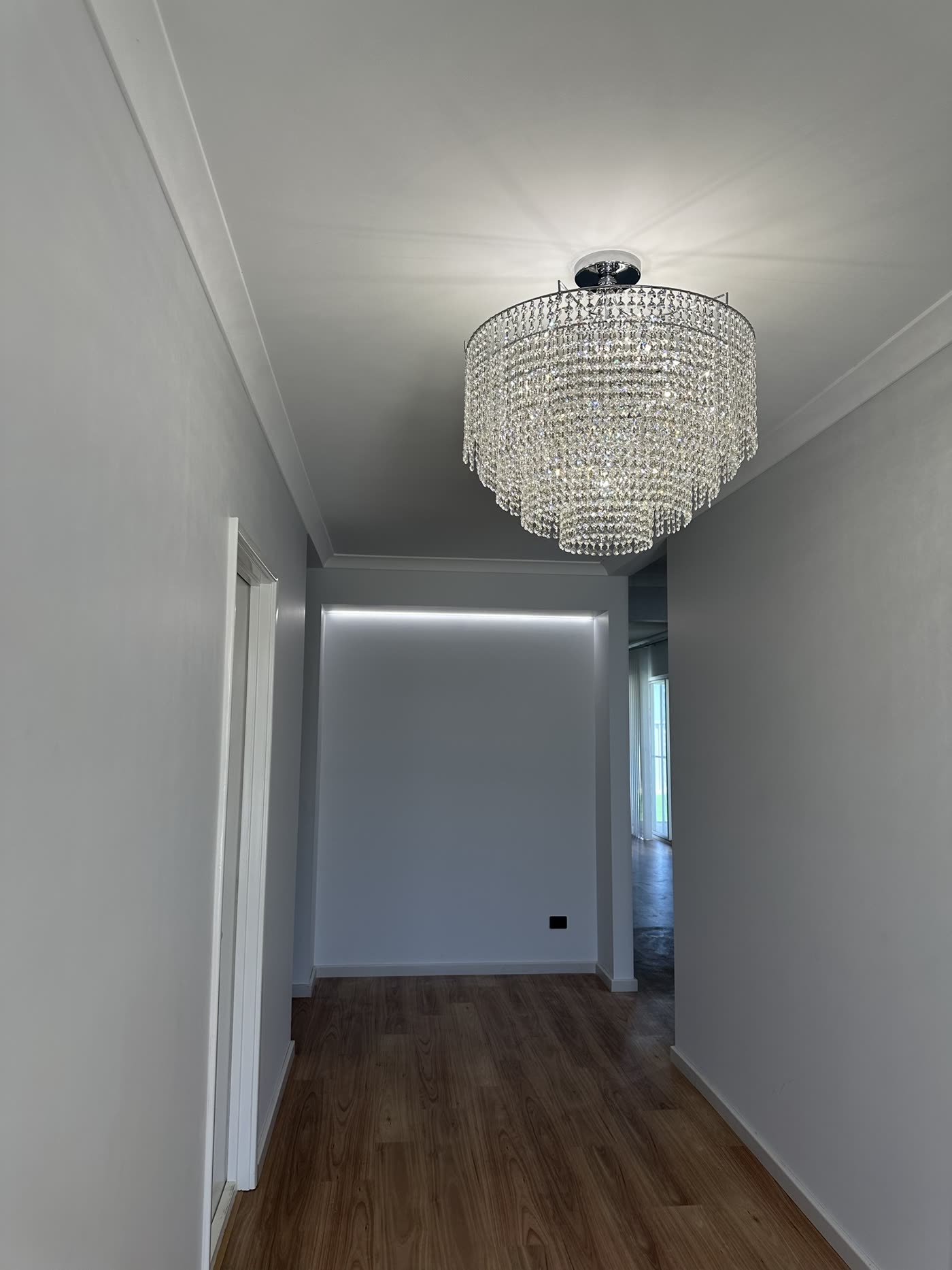 Crystal chandelier in a hallway with a recessed LED strip light on the end wall